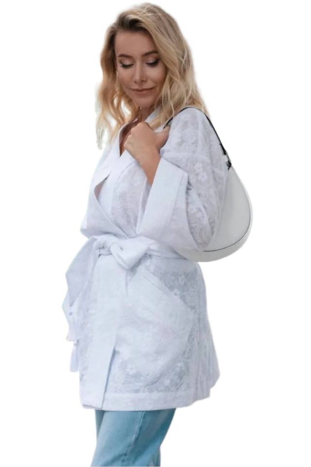 Woman wearing a light gray lace blouse and blue jeans outdoors.