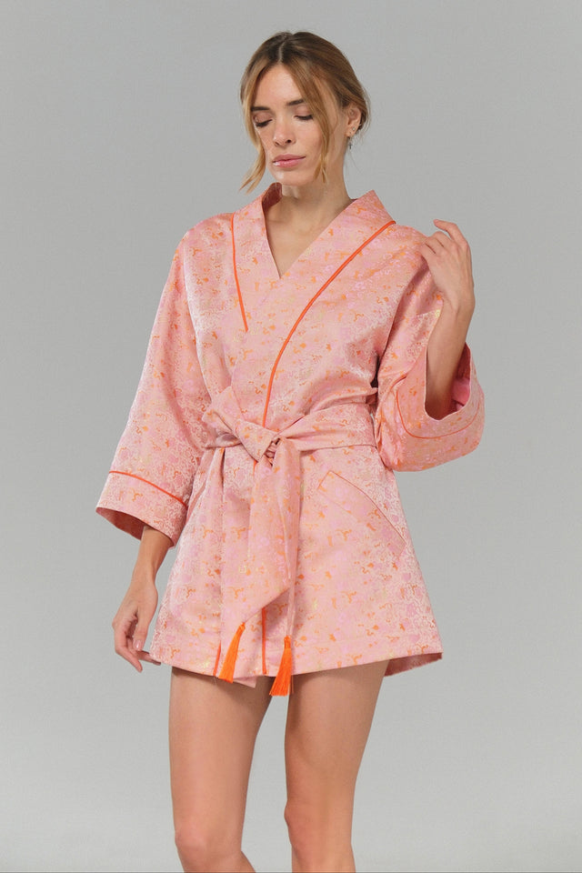 Woman wearing a pink robe with orange trim on a gray background